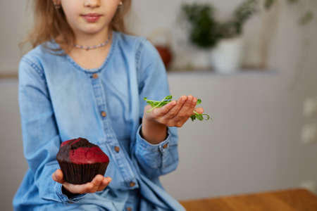 Little girl comparing food, choosing microgreen against sweet cake, Healthy dieting habit, concept of proper nutrition, the right choice foodの写真素材