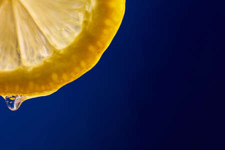 Fresh slice of lemon juice drip on blue background, citrus dripping isolated, copy space.の写真素材