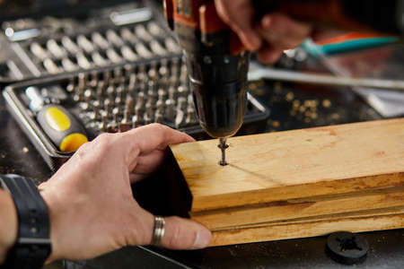 Close up of man hand drilling into wood self-tapping screw twisted into place, Power electric...