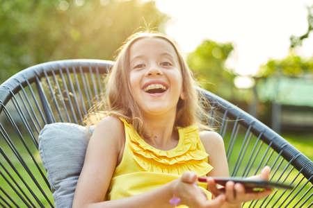 Happy kid girl playing game on mobile phone in the park outdoorの写真素材