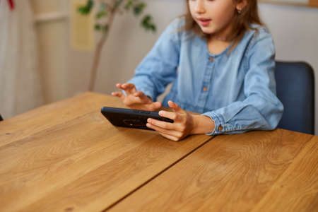 Happy kid girl playing game on mobile phone at home, child using smartphone, smartphone addiction, emotional girl.の写真素材