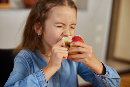 Cute little girl eat red apple at home at kitchen interior, yummy, happy child, Healthy nutrition diet vegetarian food lifestyle.の写真素材