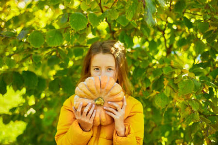 Happy child girl covers the face with pumpkin outdoors in halloweenの写真素材