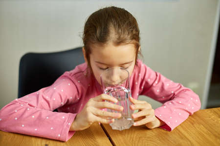 Close up of happy little girl drinking glass fresh water in kitchen, child recommend daily dose of clean aqua, dehydration, healthy lifestyle concept, Smiling To Cameraの写真素材