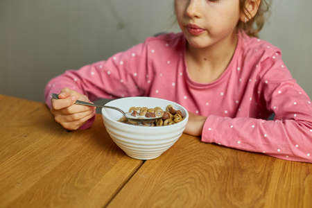 Cute little girl enjoy eating cereal with milk for morning breakfast with appetite, How tasty healthy food, Slow motion of beautiful child having breakfast at home.の写真素材