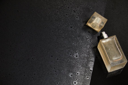 Transparent glass cosmetic perfume bottle on the dark background with water drops. Top view