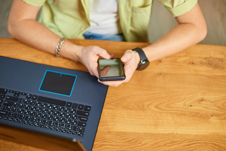 Businessman holding smartphone sitting in office, using cell phone mobile apps and laptop, types a message with a smartphone, man downloading in mobile store popular applicationsの写真素材