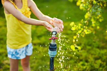 Happy kid girl playing by hand with garden sprinkler , summer outdoor water fun in the backyard at home, splash on sunny day.の写真素材