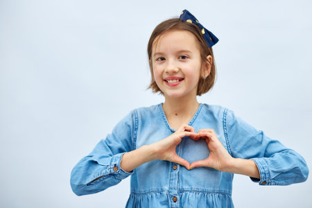 Smiling little girl make heart sign with hands in casual denim dress isolated on white background, studio, makes love icon, gesture with fingers Heart symbol, love concept.の写真素材