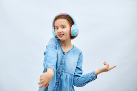 Girl teenager in casual denim dress listening to music in headphones on white background, wireless earphones enjoying music dancing , Modern technology, Protect Developing Earsの写真素材