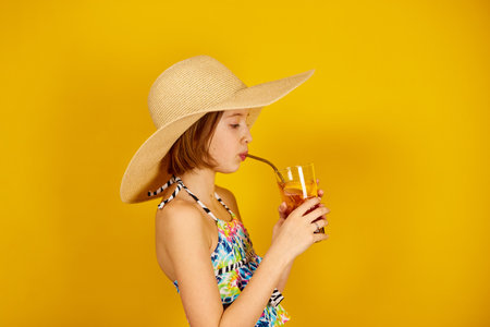 Child teenager girl in swimsuit and straw hat with lemonade metal straw in studio on yellow background, summer mood,の写真素材