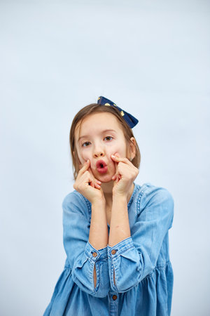 Smiling little girl make trend mini heart sign with fingers in casual denim dress isolated on white...