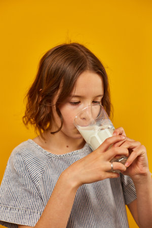 Pretty teen girl, child with a fresh glass of milk isolated on studio yellow background, strong bones, milk for growth, healthy lifestyle concept, copy spaceの写真素材