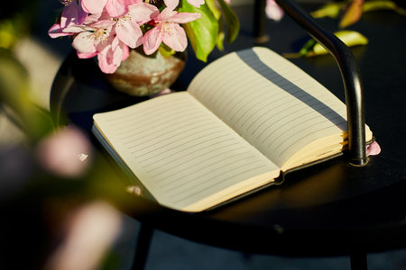 Open notebook and flowers and on the small black table on terrace at home in a sunny day, hardlight, outdoor workspace, summer relaxation, notes, ideas, planningの写真素材