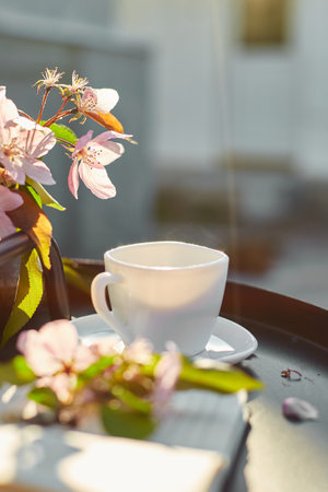 Cup of coffee with steam flowers and notebook on the small black table on terrace at home in a sunny day, outdoor workspace, summer relaxation, coffee break.の写真素材