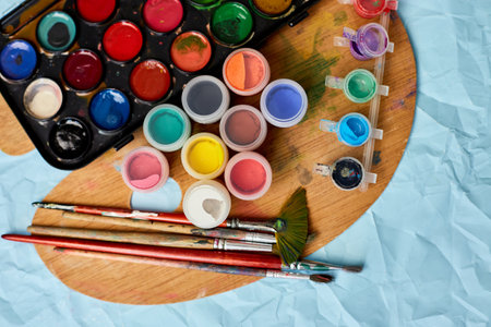 Flat lay of colorful paints, painting palette and brushes on blue background, art, painting and hobby concept, top view, copy space.の写真素材