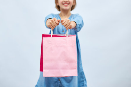 Pretty child girl in casual denim dress hold in hand pink shopping bags on white background, studio, Shopaholic shopping and fashion, discount sale concept, copy space, banner. Black fridayの写真素材