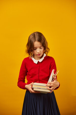 Portrait of happy schoolgirl reading a book on yellow studio background, educatin concept, Back to School, copy space, Teenager girl in school uniform.の写真素材