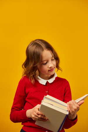 Portrait of happy schoolgirl reading a book on yellow studio background, educatin concept, Back to School, copy space, Teenager girl in school uniform.の写真素材