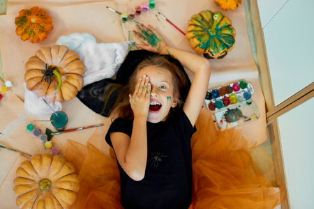 Top view of Smiling girl lying on the floor between drew pumpkin Halloween, and decoration for party, paint hands, emotion, make faces.の写真素材