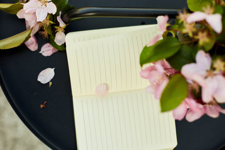 Open notebook and flowers and on the small black table on terrace at home in a sunny day, outdoor...