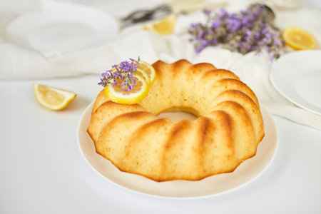 Round lemon cake on white table with lavender flower bouquet