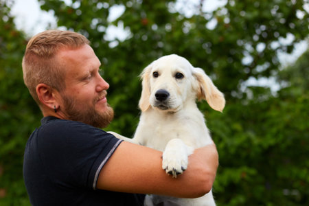 Man Smiling While Holding A Playful Golden Retriever Puppy Outdoors In Summerの写真素材