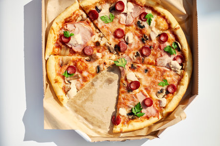 A freshly baked pizza with sliced tomatoes, cheese, mushrooms, and herbs is missing two slices, suggesting a shared meal at an outdoor picnic.の写真素材