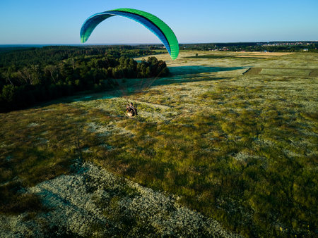 Paraglider Soaring High Above Lush Green Fields on a Sunny Day