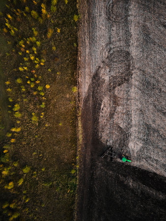 Tractor cultivating vast farmland, creating a contrast between tilled soil and untouched terrain.