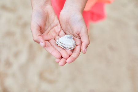 A child cradles a delicate seashell in their hands on a sandy shore.