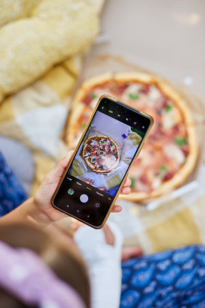 Girl snaps a picture of a delicious pizza using a phone, while wearing a cast on one arm.