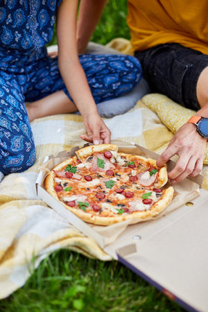 Father and daughter enjoying a pizza together while sitting on a picnic blanket.の写真素材