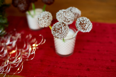 Chocolate cake pops with coconut shavings are displayed in a glass at a celebration, surrounded by festive decorations.の写真素材