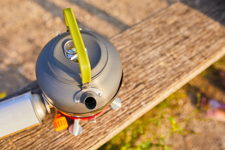 A kettle is placed on a portable stove near a serene lake while the sun sets in the background. The warm glow enhances the calm atmosphere, ideal for outdoor cooking.の写真素材