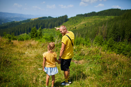A father and his daughter share a moment in the mountains, with him pointing towards the scenic view. They enjoy their time together in nature, building memories and exploring trails.の写真素材