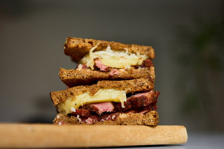 Two layers of a Reuben sandwich filled with corned beef, Swiss cheese, and sauerkraut, placed on a wooden board, highlighting a tasty meal perfect for lunchtime.の写真素材