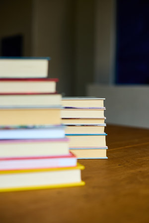 A collection of colorful books stacked neatly on a wooden table, evoking a sense of warmth and inviting readers to explore the stories within them.の写真素材