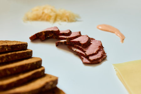 Sliced rye bread, corned beef, cheese, sauerkraut, and dressing are artfully displayed on a white surface, inviting assembly into a delicious Reuben sandwich ingredientsの写真素材