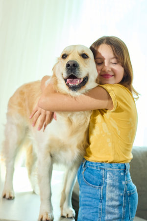 A young girl with brown hair smiles as she hugs a golden retriever standing on a couch. The well-lit living room adds warmth to their joyful moment together.の写真素材