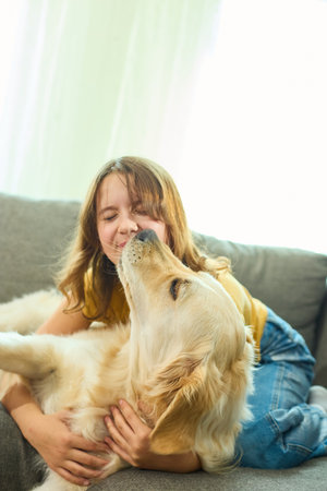Teen girl plays joyfully with her golden retriever in a bright living room during a sunny afternoonの写真素材