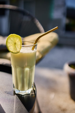 Glasses of lime and condensed milk cocktails sit on a black table in a sunlit terrace. Fresh lime wedges garnish each drink, highlighting a casual summer vibe.の写真素材