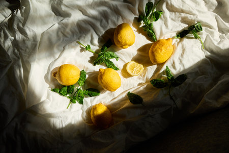 A collection of fresh lemons and vibrant basil leaves is artistically arranged on a light fabric background, showing the essence of summer in Italy, highlighting their natural beauty.の写真素材