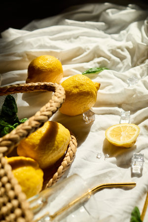 Lemons rest in a woven bag alongside fresh mint leaves and glassware, creating a vibrant summer feel on a sunlit cloth backdrop in Italy.の写真素材