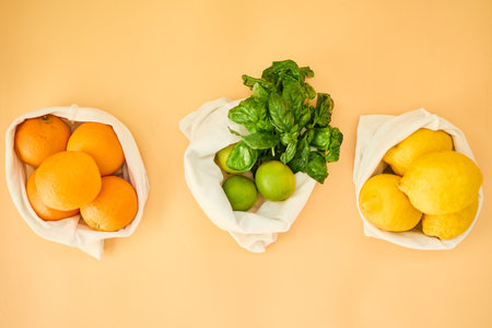 Colorful fruits and herbs are arranged in reusable cloth bags on a pastel background, highlighting...