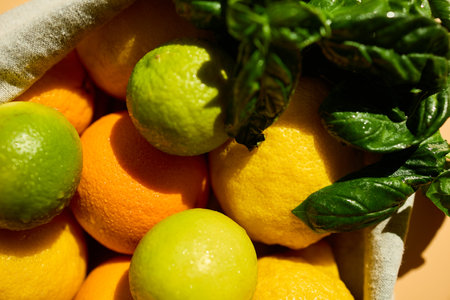 A reusable basket holds vibrant yellow lemons, oranges, and green limes, along with fresh basil leaves, promoting eco-friendly grocery shopping and healthy living.の写真素材