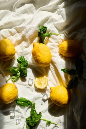 A collection of fresh lemons and vibrant basil leaves is artistically arranged on a light fabric...