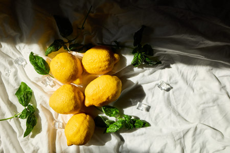 A collection of fresh lemons and vibrant basil leaves is artistically arranged on a light fabric...