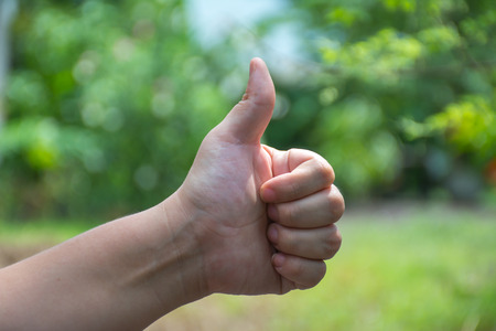 Plump body women hand showing thumb up, with nature blur in background