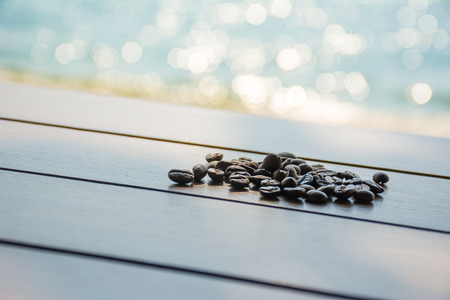 Coffee bean on wooden table with sea blurred in backgroundの写真素材